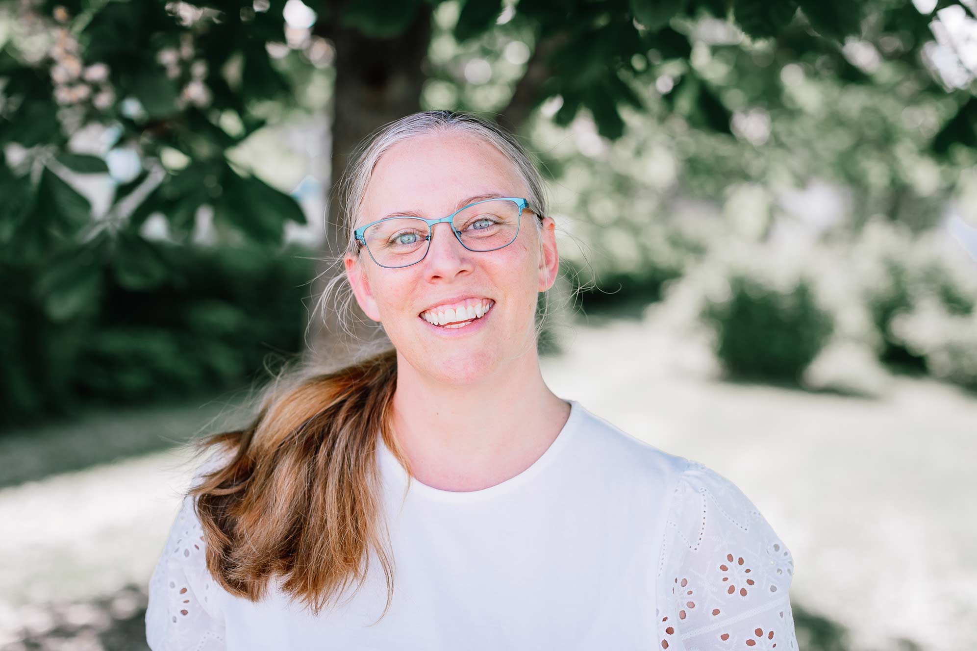 Maria Åkerblom, ägare av kommunikationsbyrån Åkerblom Kommunikation i Nyköping, står under ett träd och ser glad och välkomnande ut.